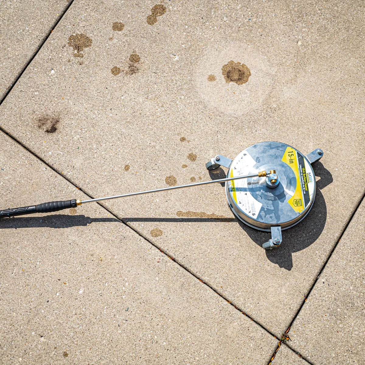 Sparkle Service employee pressure washing a large concrete surface with a surface cleaner