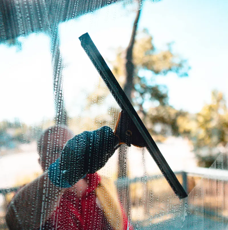 A technician pulling a squeegee down a soapy window in warm light