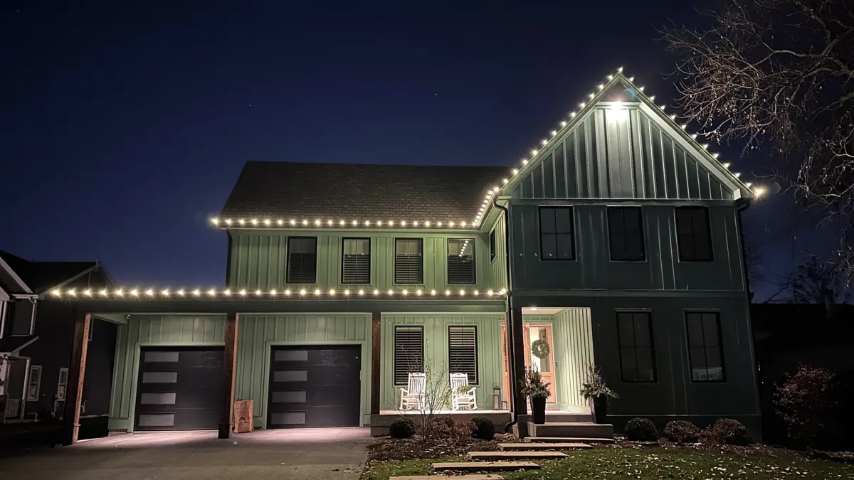 Warm white C9 holiday lights along the rooflines of a modern green farmhouse at night