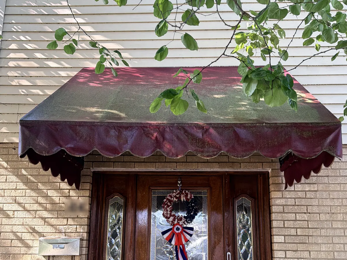 A dark red fabric door awning before cleaning, the top panel covered in green algae and grey soil